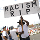 A man carries a ‘Racism RIP’ sign at a makeshift memorial honoring victims outside Walmart, near the scene of a mass shooting which left at least 22 people dead, on Aug. 6, 2019, in El Paso, Texas. A 21-year-old white male suspect remains in custody.